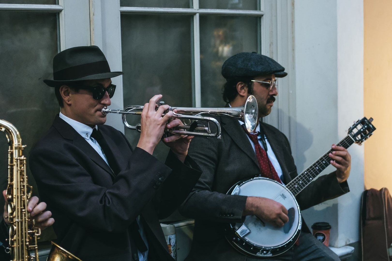 Zwei Musiker in Anzügen spielen Trompete und Banjo vor einem Fenster